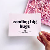 Greeting card with 'sending big hugs' text, with pink shredded paper in the background.